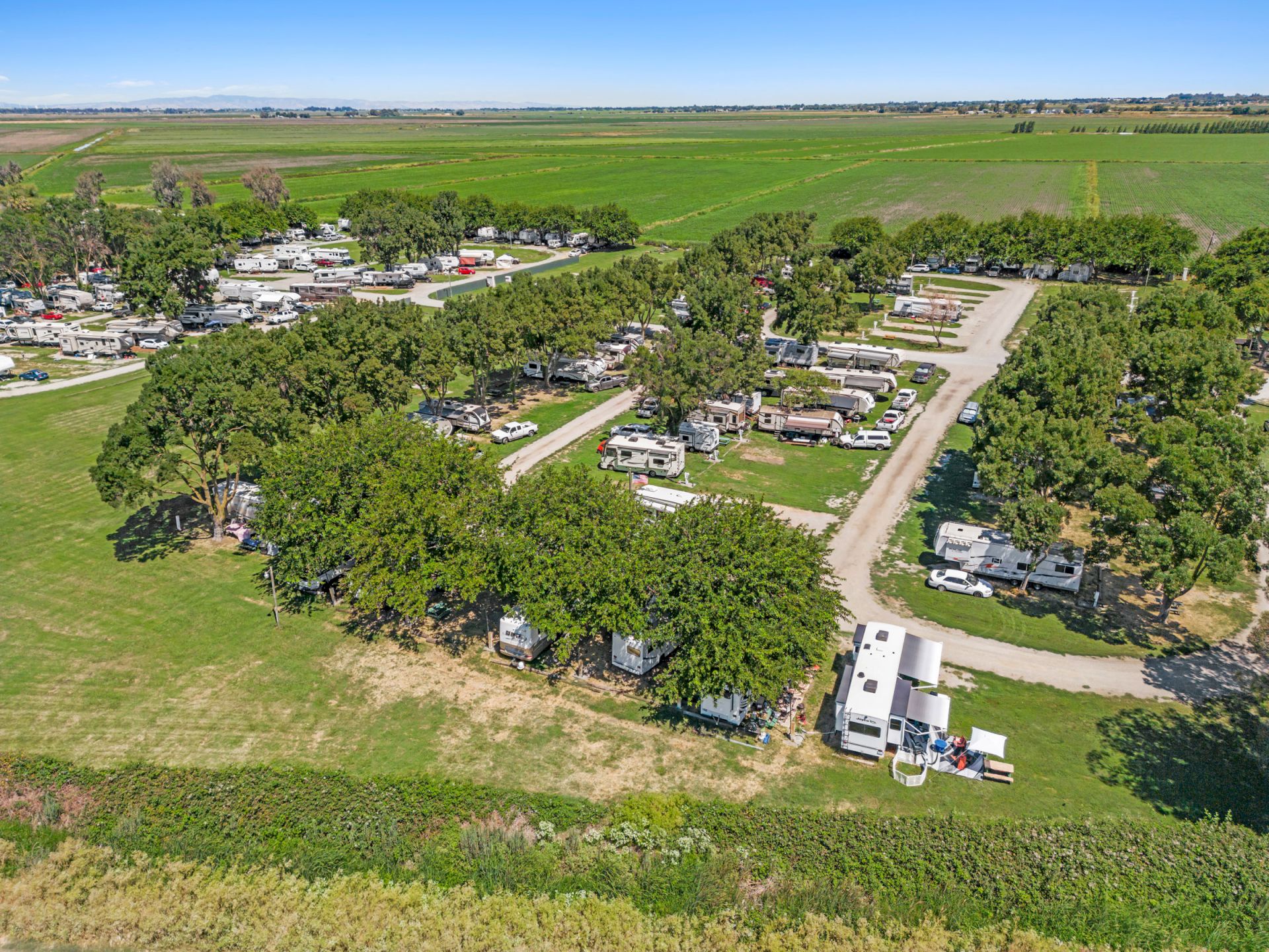 The image shows an aerial view of a campsite or RV park with several trailers surrounded by trees and fields in a rural area.