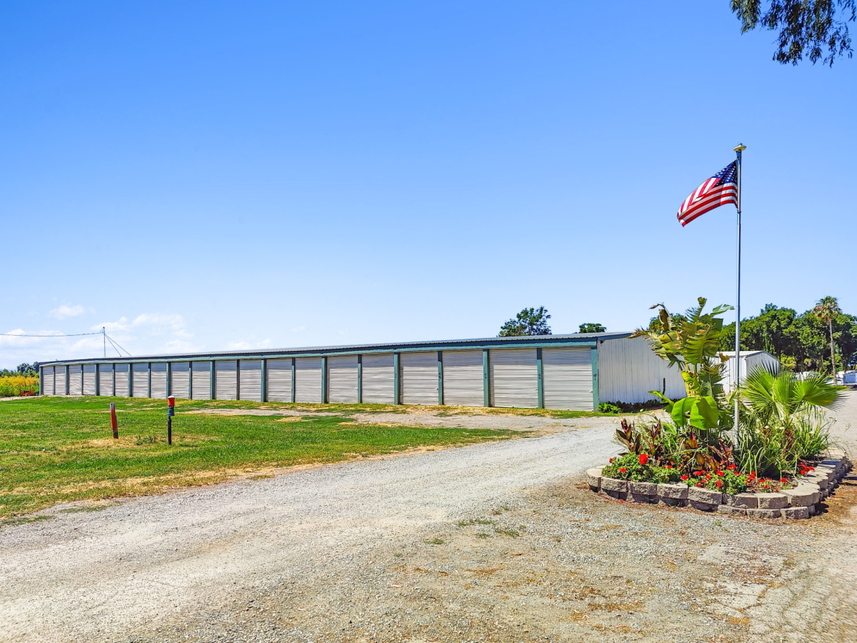 A storage facility with multiple units, a gravel path, and a U.S. flag on a pole in a landscaped area.