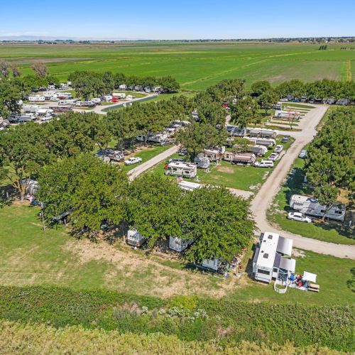 An aerial view of a campground with RVs and trees, surrounded by green fields, under a clear sky.