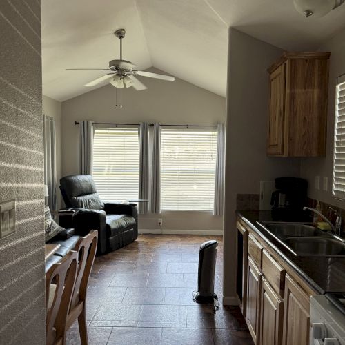 A small, cozy room with a kitchen on the right, dining table on the left, and a seating area with windows in the back.
