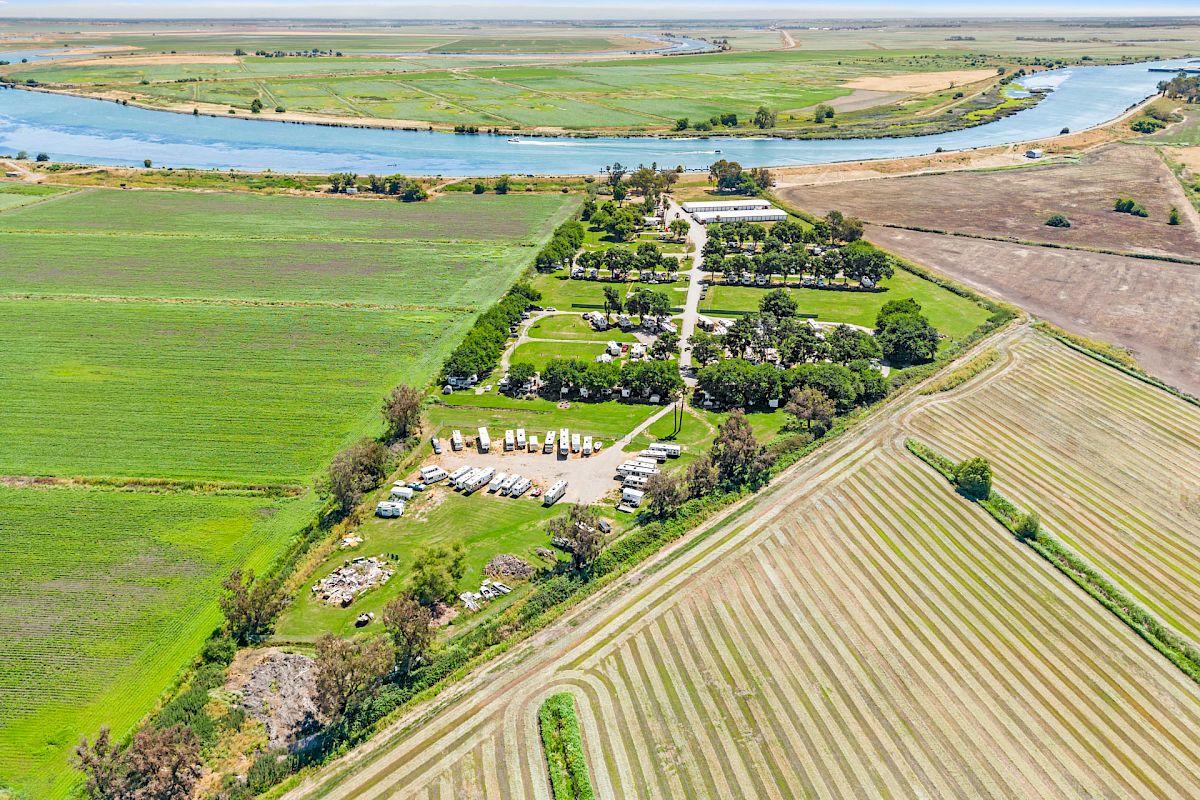 An aerial view of a green landscape with fields, a river, and a roadway passing through, surrounded by lush vegetation and clear skies.