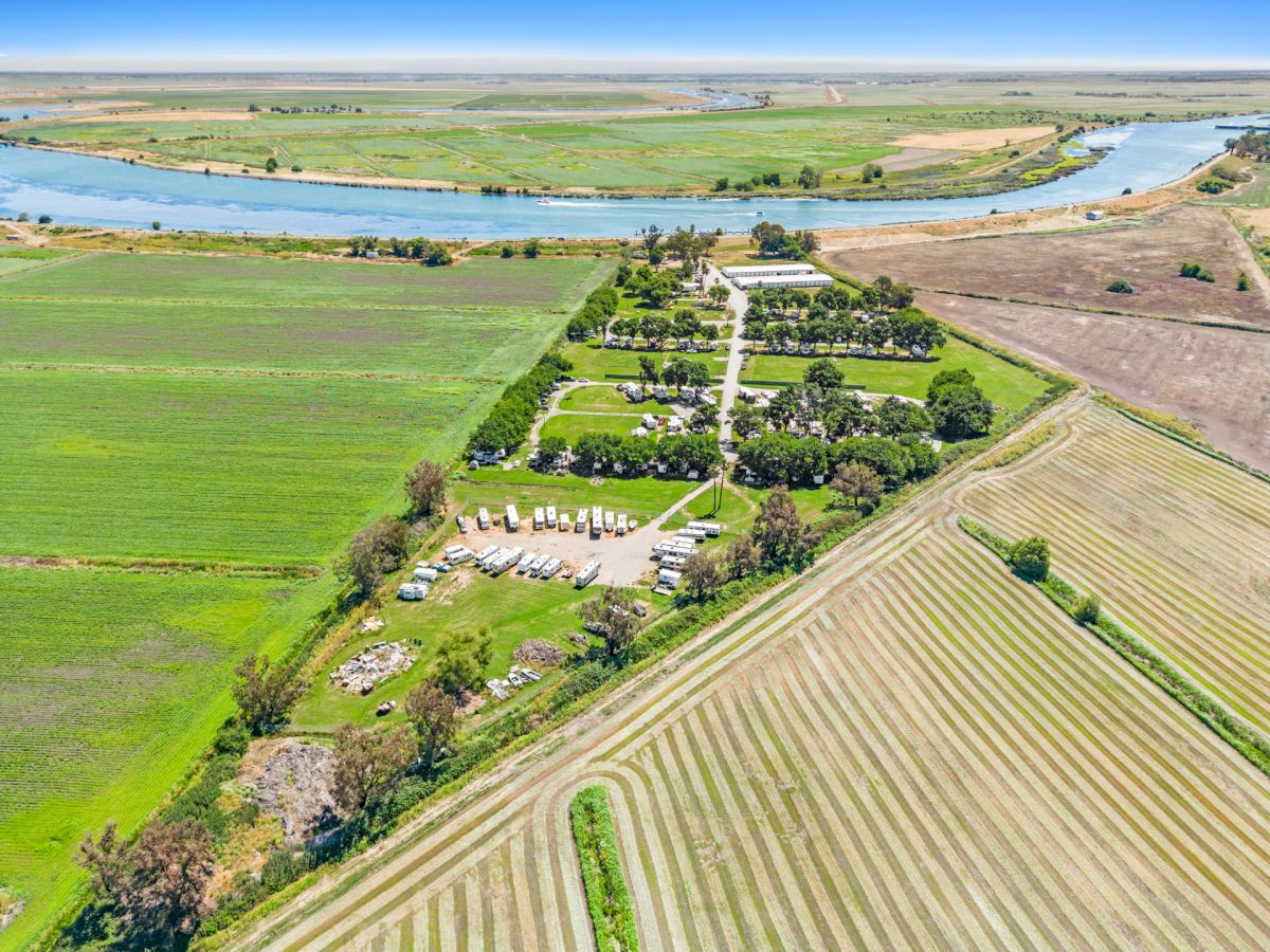An aerial view of a green landscape with fields, a river, and a roadway passing through, surrounded by lush vegetation and clear skies.