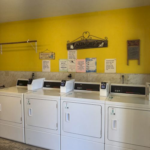 Four white laundry machines are in a room with yellow walls and various signs above them.