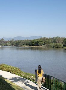 A scenic lakeside with clear water, a person standing on a jetty, and a tree-lined shore in the background.