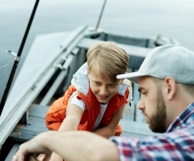 A father and son fishing from a boat, sharing a moment of teamwork and summer fun on the water.