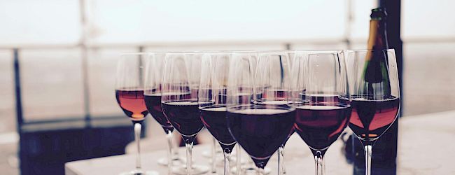 A row of empty wine glasses on a black tray, with a bottle and a blurred, light-colored background.