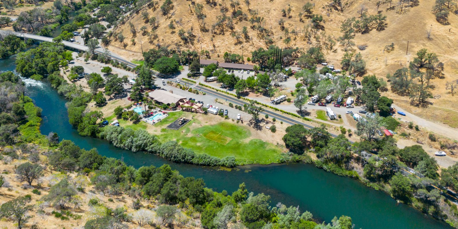 A scenic river winds through a desert canyon with a green embankment, a small town along the shore, and rugged hills in the background.